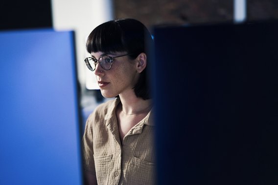 Eine junge Frau blickt auf zwei Bildschirme und arbeitet in einem digitalen Workflow