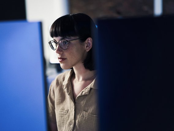 Sichere IT-Geschäftsprozesse in Unternehmensorganisationen Eine junge Frau blickt auf zwei Bildschirme und arbeitet in einem digitalen Workflow